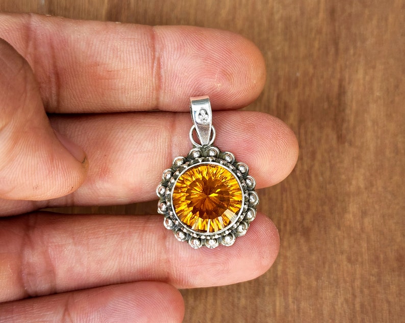 May include: A silver pendant featuring a round, faceted, orange gemstone set in a silver bezel with a beaded border.