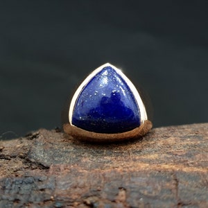 Pode incluir: Um anel de ouro com uma gema triangular de lapis-lazúli azul.