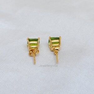 May include: A pair of gold earrings with green gemstone accents. The earrings have a post back closure.