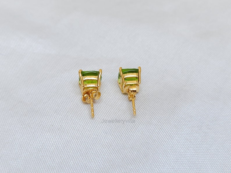 May include: A pair of gold earrings with green gemstone accents. The earrings have a post back closure.