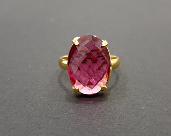 Könnte beinhalten: Goldener Ring mit einem großen, oval geschliffenen Edelstein in Rosa- und Rottönen. Der facettierte Stein wird von vier Krappen gehalten. Das Band des Rings ist aus poliertem Gold gefertigt.