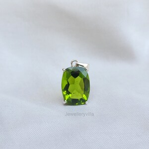 May include: A green gemstone pendant with a silver setting. The gemstone is a cushion cut and has a shiny, polished finish.