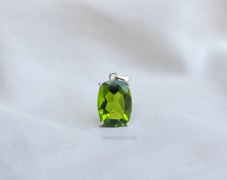 May include: A green gemstone pendant with a silver setting. The gemstone is a cushion cut and has a shiny, polished finish.