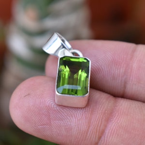 Puede incluir: Un colgante de plata con una piedra preciosa verde. La piedra preciosa est&aacute; tallada en forma rectangular con bordes biselados.