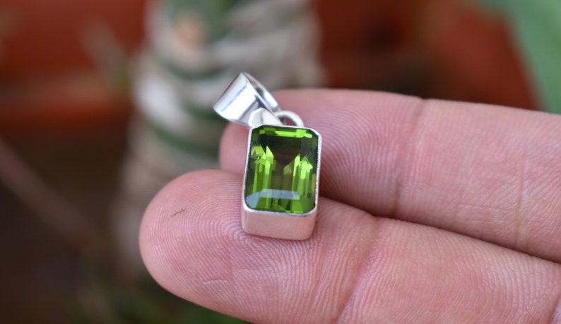 Puede incluir: Un colgante de plata con una piedra preciosa verde. La piedra preciosa est&aacute; tallada en forma rectangular con bordes biselados.