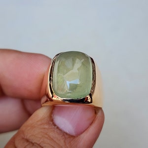 Puede incluir: Un anillo de oro con una piedra rectangular grande de color verde claro.