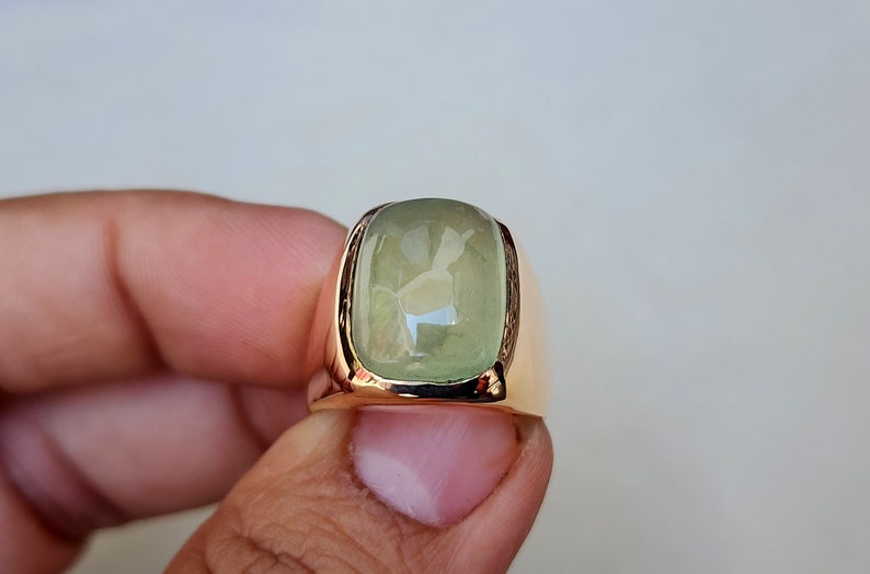 Puede incluir: Un anillo de oro con una piedra rectangular grande de color verde claro.