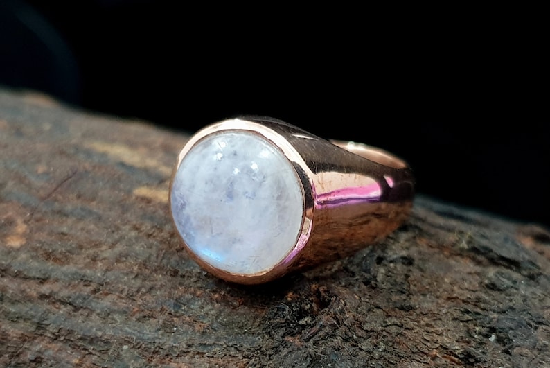 Puede incluir: Un anillo de oro rosa con una gran piedra de luna redonda y blanca.