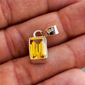 May include: A silver pendant with a rectangular, yellow gemstone. The pendant has a 925 stamp on the bail.