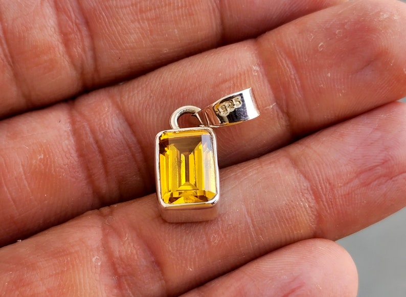 May include: A silver pendant with a rectangular, yellow gemstone. The pendant has a 925 stamp on the bail.
