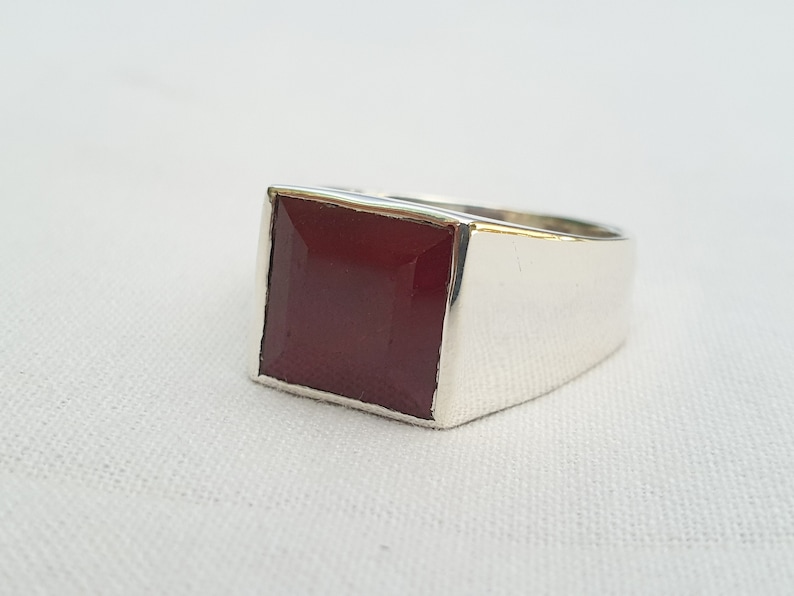 Peut inclure: Une bague en argent avec une pierre carr&eacute;e rouge fonc&eacute;.