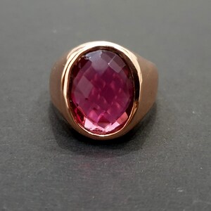 May include: A rose gold ring with a large, faceted, oval-shaped, pink gemstone.