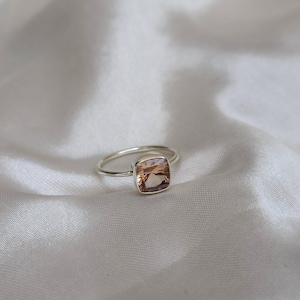 May include: A silver ring with a square-shaped, light brown gemstone.