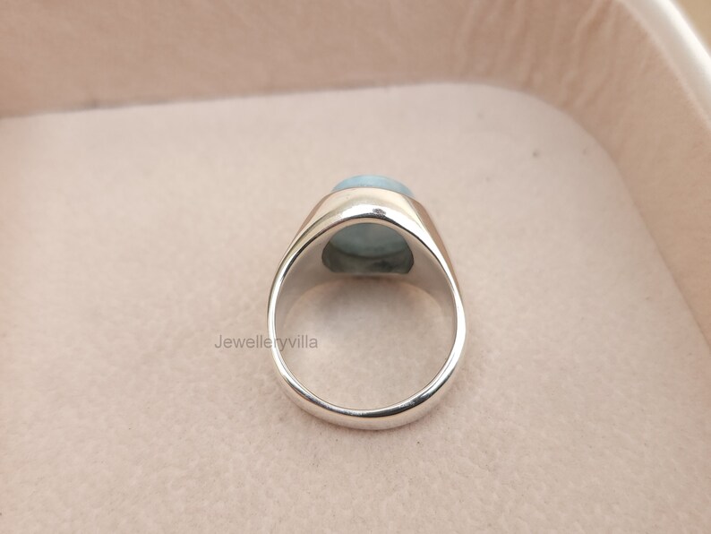 K&ouml;nnte beinhalten: Ein silberner Ring mit einem hellblauen ovalen Edelstein, der in einer Zargenfassung sitzt. Der Ring wird von hinten gezeigt.