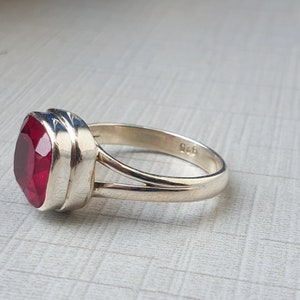May include: A silver ring featuring a red gemstone. The ring is hallmarked with "925" on the inside of the band.
