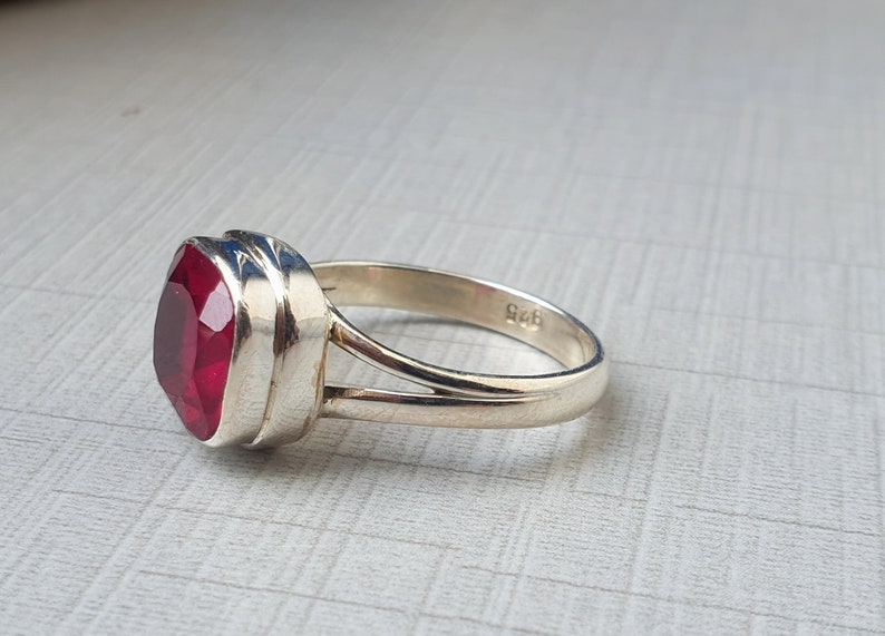 May include: A silver ring featuring a red gemstone. The ring is hallmarked with "925" on the inside of the band.