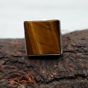 May include: A square-shaped ring with a brown tiger's eye gemstone set in a silver band.