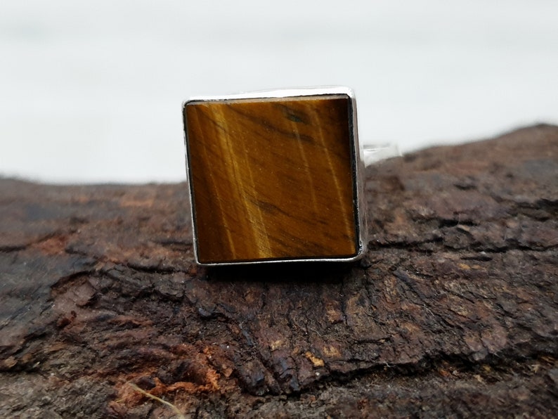 May include: A square-shaped ring with a brown tiger's eye gemstone set in a silver band.