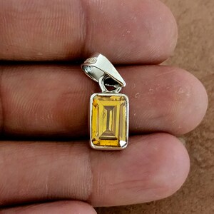 May include: A silver pendant with a rectangular, faceted, yellow gemstone.