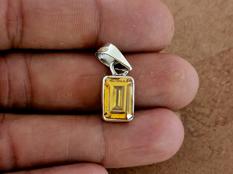May include: A silver pendant with a rectangular, faceted, yellow gemstone.
