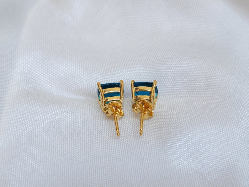 Puede incluir: Un par de pendientes de oro con detalles de piedras preciosas azules. Los pendientes tienen cierre de poste.
