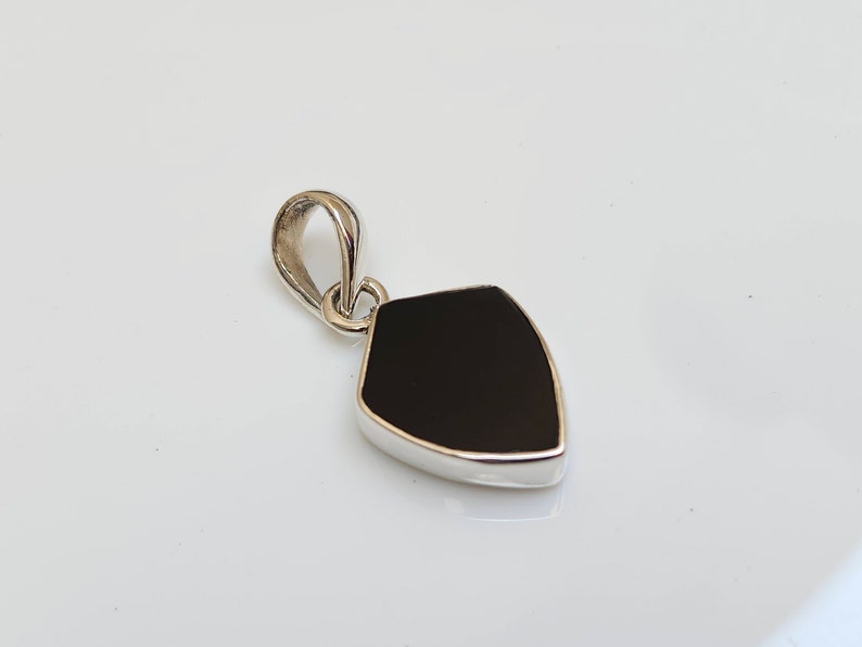 May include: A silver pendant with a black gemstone in the shape of a shield.