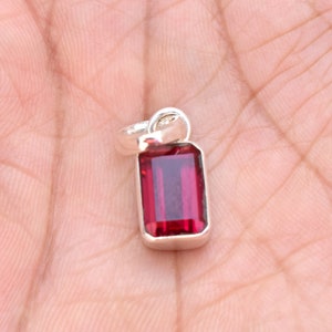 May include: A silver pendant featuring a red gemstone in a rectangular shape.