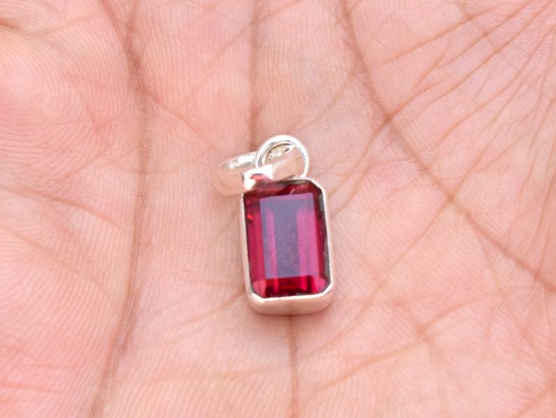 May include: A silver pendant featuring a red gemstone in a rectangular shape.