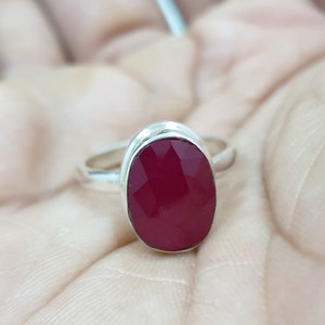 May include: A silver ring with a large, oval-shaped, faceted, dark red gemstone.