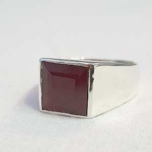 Peut inclure: Une bague en argent avec une pierre pr&eacute;cieuse carr&eacute;e rouge fonc&eacute;.