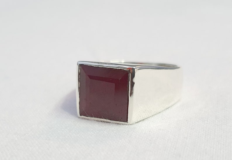 Peut inclure: Une bague en argent avec une pierre pr&eacute;cieuse carr&eacute;e rouge fonc&eacute;.