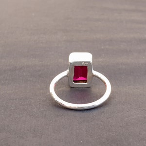 Op de afbeelding: Een zilveren ring met een rechthoekige roze edelsteen gezet in een zilveren bezel. De ring heeft een eenvoudige band.