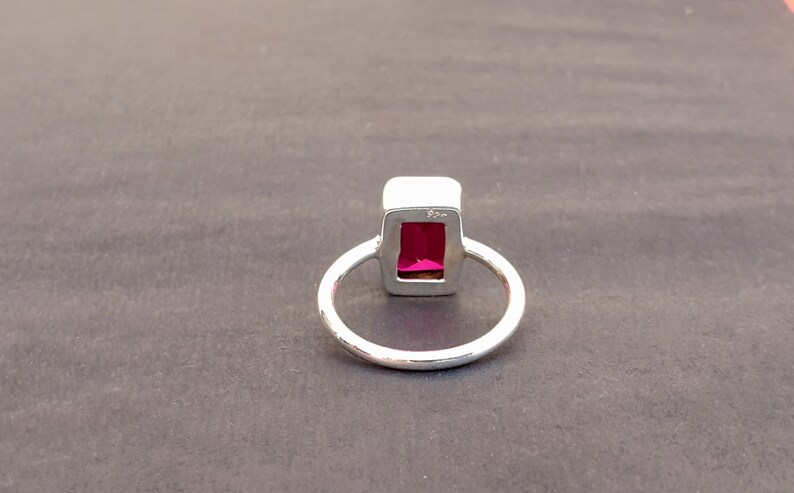 Op de afbeelding: Een zilveren ring met een rechthoekige roze edelsteen gezet in een zilveren bezel. De ring heeft een eenvoudige band.
