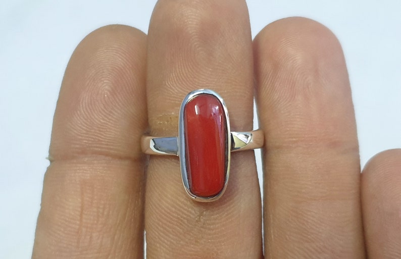 May include: A silver ring with a red oval-shaped gemstone.