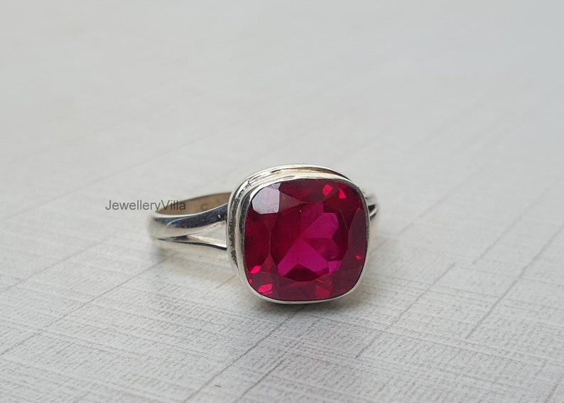 May include: A silver ring featuring a large, square-shaped, bright red gemstone.