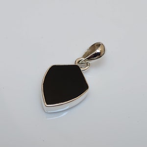 May include: A black gemstone pendant with a silver setting. The pendant is shaped like a shield and has a smooth, polished surface.