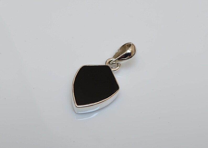May include: A black gemstone pendant with a silver setting. The pendant is shaped like a shield and has a smooth, polished surface.