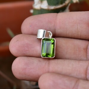 Puede incluir: Un colgante de plata con una piedra preciosa verde. La piedra preciosa es rectangular y tiene un corte facetado.