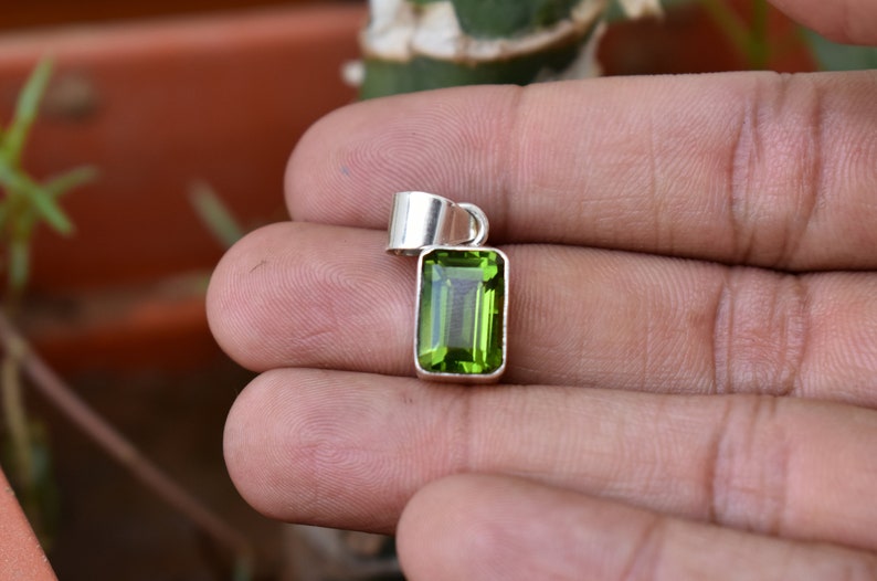 Puede incluir: Un colgante de plata con una piedra preciosa verde. La piedra preciosa es rectangular y tiene un corte facetado.