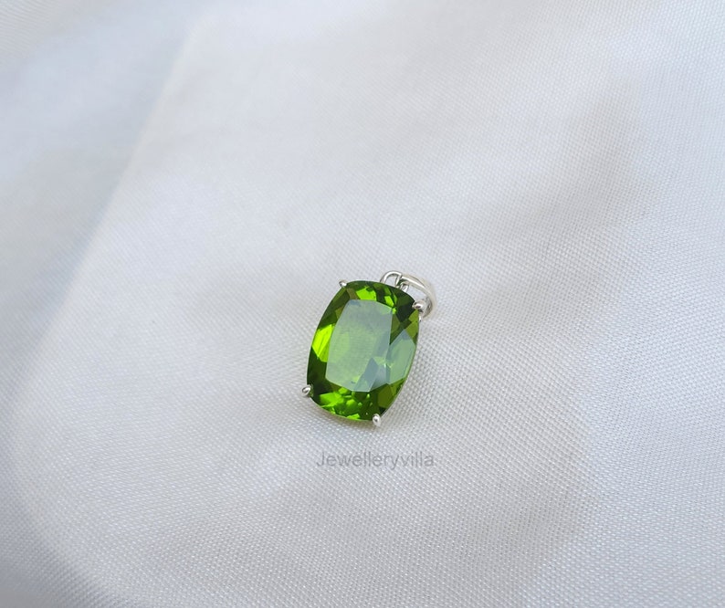May include: A green peridot gemstone pendant set in silver. The stone is a cushion cut and has a smooth, polished finish.