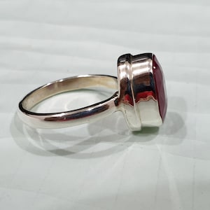 May include: A silver ring with a large, oval-shaped, dark red gemstone set in a bezel setting.
