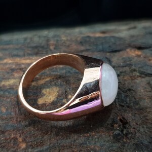 Puede incluir: Un anillo de oro rosa con una piedra ovalada blanca.