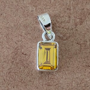 May include: A silver pendant with a rectangular, yellow gemstone. The pendant has a bail with the number "925" stamped on it.