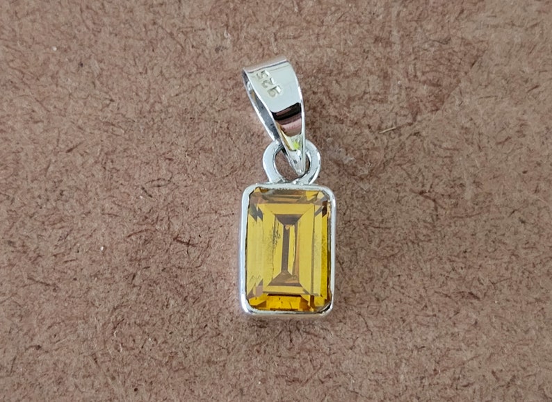 May include: A silver pendant with a rectangular, yellow gemstone. The pendant has a bail with the number "925" stamped on it.