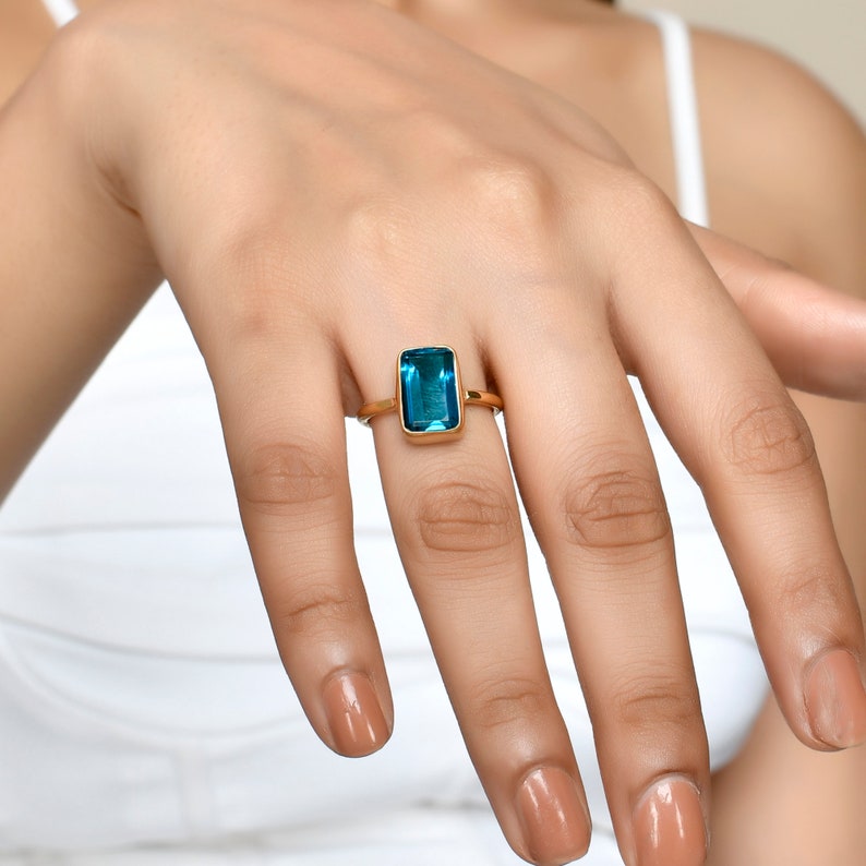 May include: A gold ring with a large, rectangular, blue gemstone.