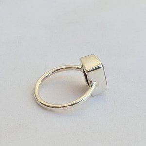 Op de afbeelding: Een zilveren ring met een rechthoekige, donkerpaarse edelsteen.