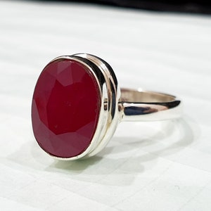 May include: A silver ring with a large, oval-shaped, red gemstone.