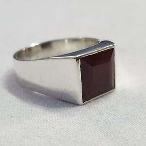 Peut inclure: Une bague en argent avec une pierre carr&eacute;e rouge fonc&eacute;.