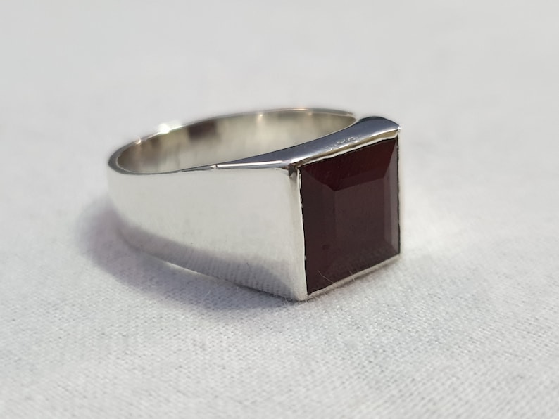 Peut inclure: Une bague en argent avec une pierre carr&eacute;e rouge fonc&eacute;.