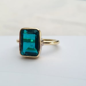 May include: A gold ring with a large, emerald green gemstone. The gemstone is cut in a rectangular shape.